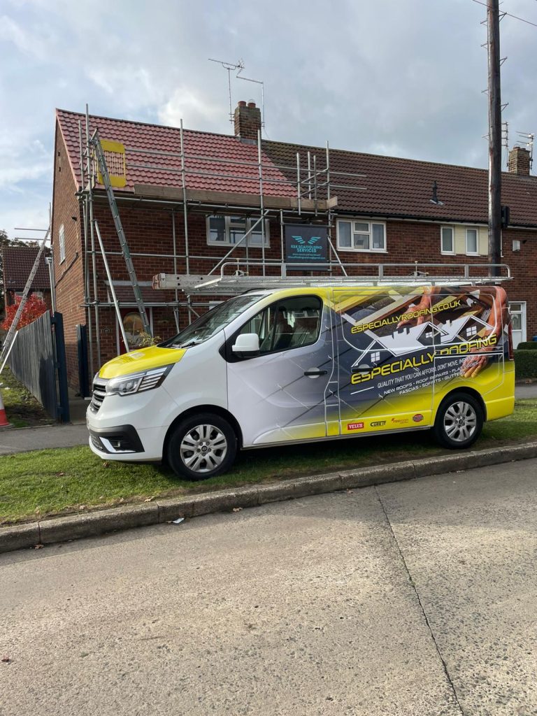 A white van with "Especially Roofing" branding is parked on the street in front of a brick house with scaffolding set up for roof work. A sign for the roofing company is displayed on the scaffolding.